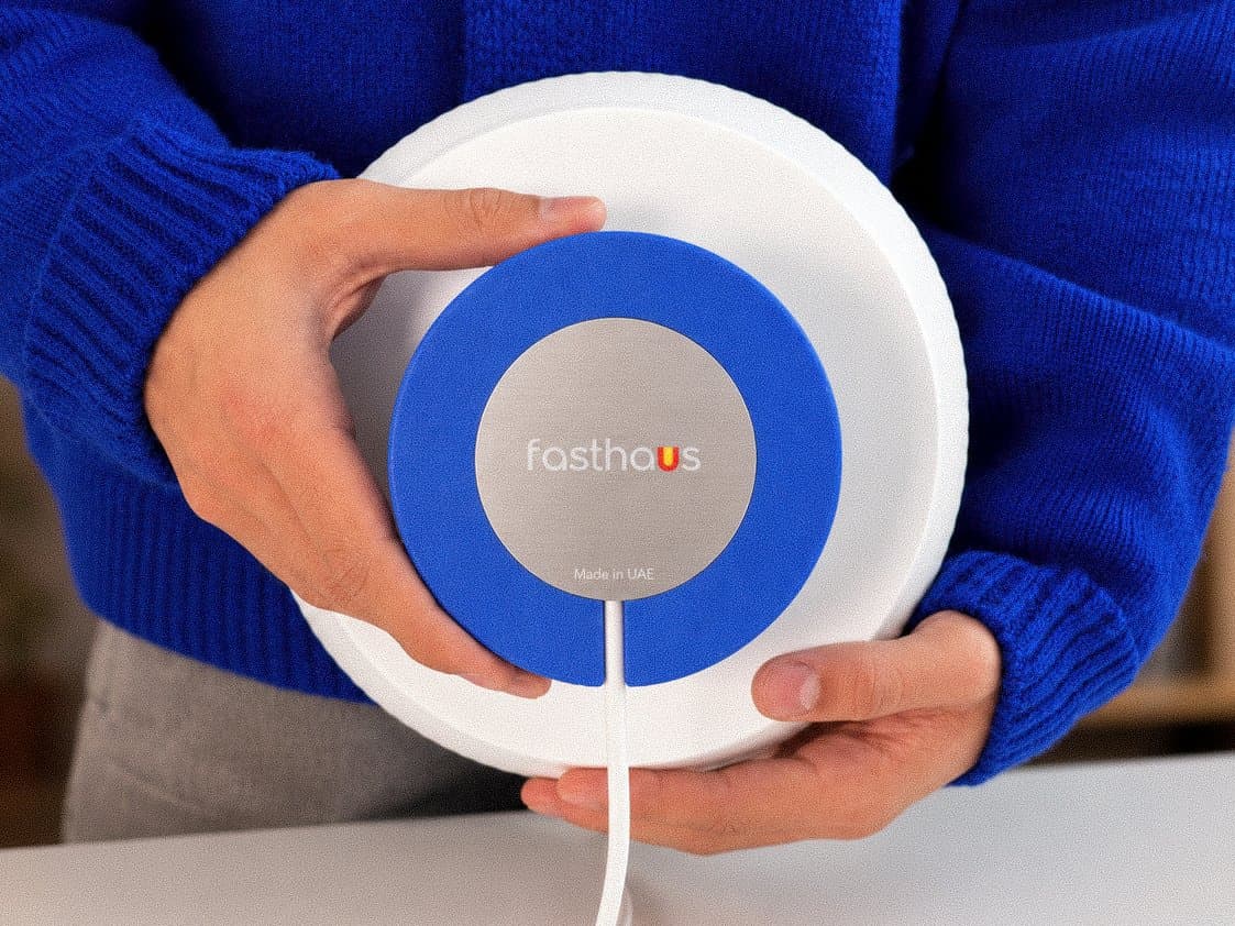 Hands holding a white Fasthaus lamp with a blue baseplate